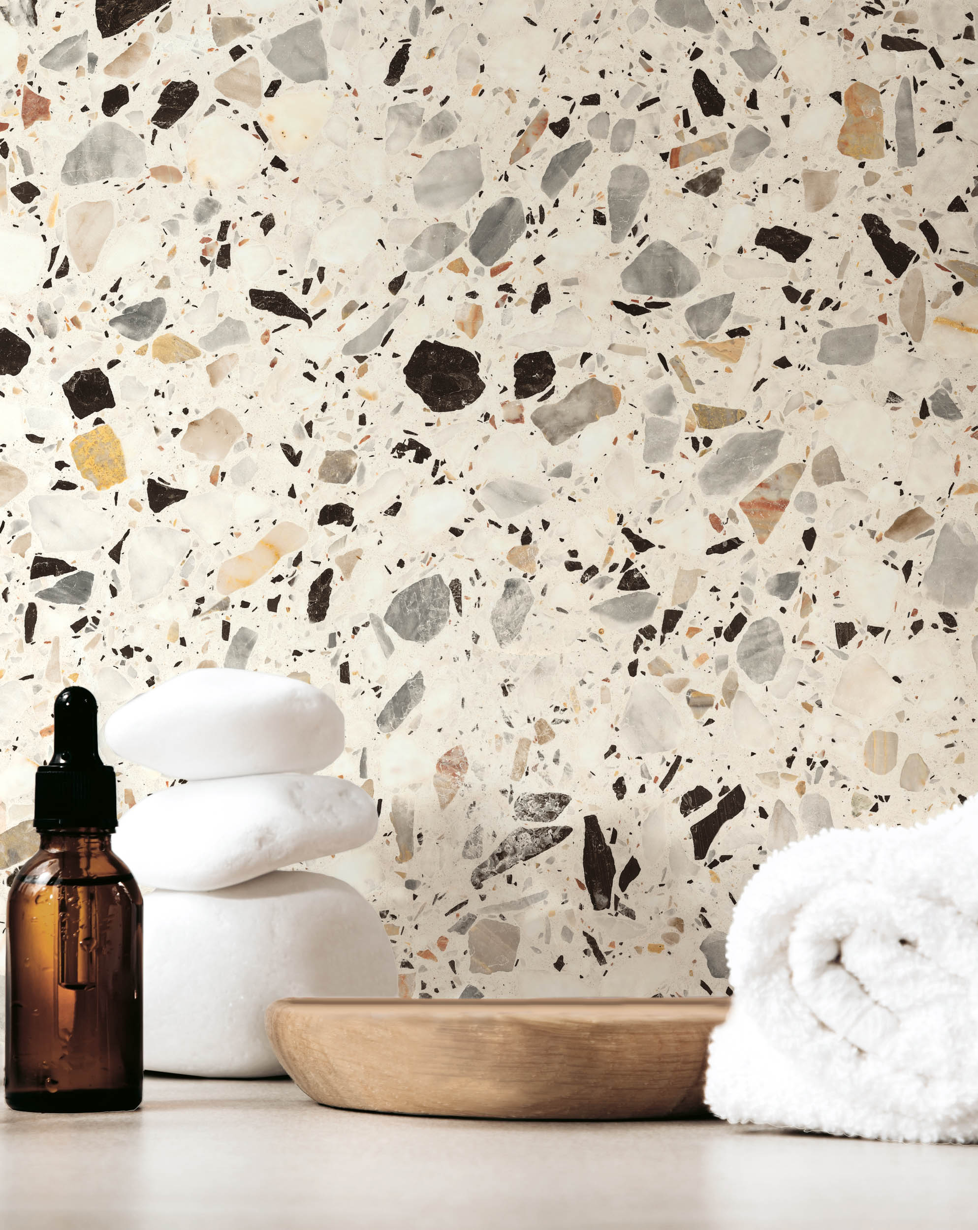 Transparent bottles with cosmetics with water drops on a wooden plate with a face roller and a towel on a beige background with white smooth stones. Front view