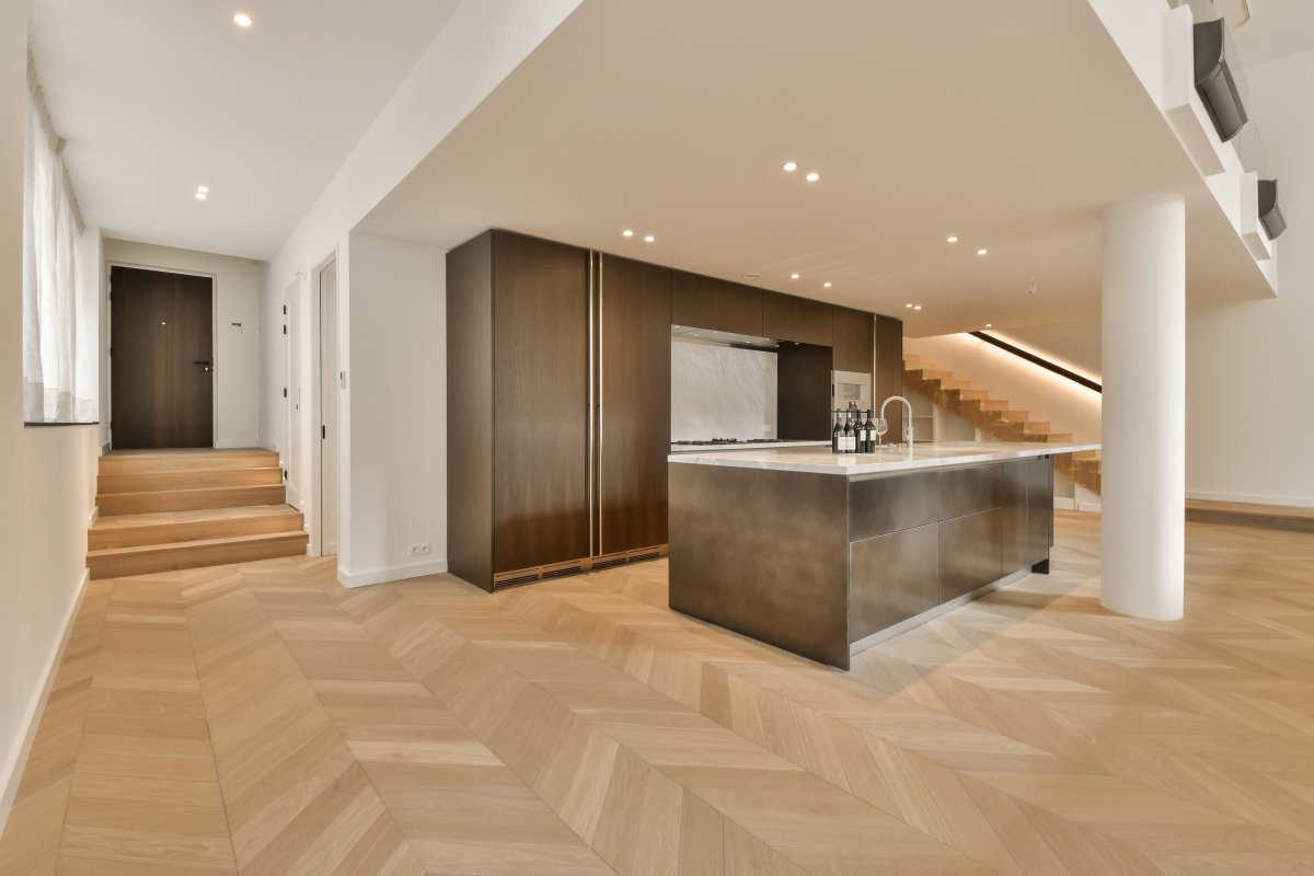 a modern kitchen and living room in an apartment with wood flooring, white walls and wooden staircase leading up to the second floor