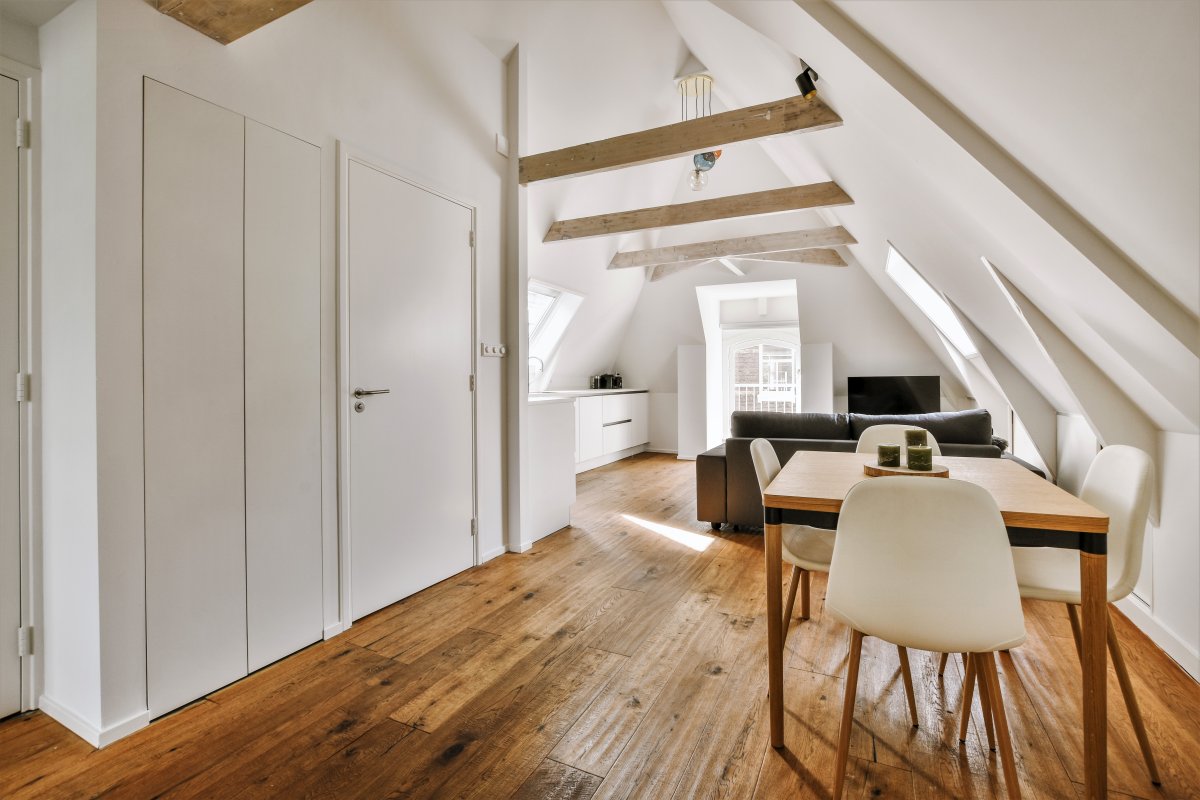 Contemporary minimalist style interior design of light studio apartment with wooden table and chairs in dining zone between open kitchen and living room with white walls and parquet floor